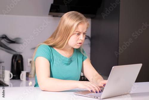 Young concentrated blonde woman working with laptop in her apartment. Stay at home concept. Copy space. Girl working, learning online.