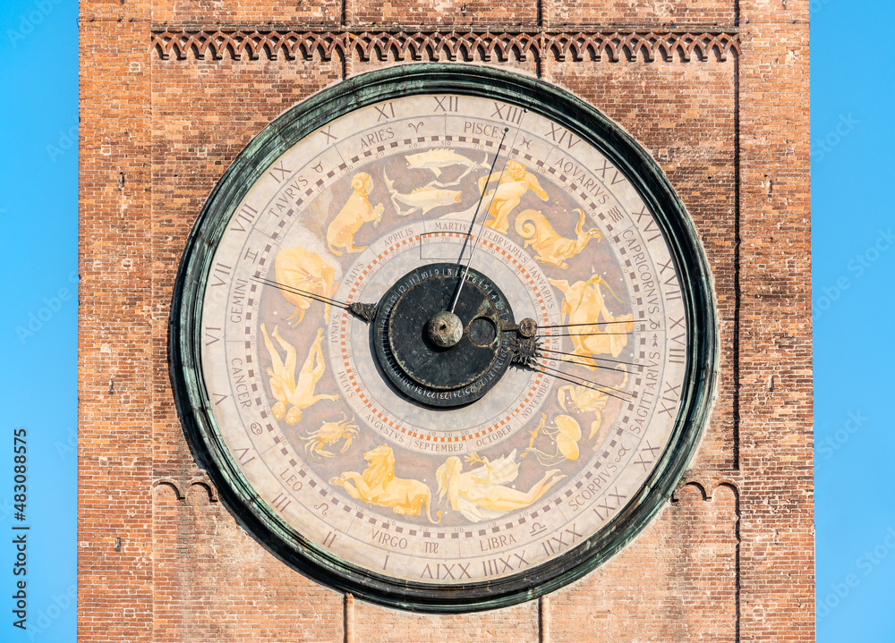 A huge unusual dial of an old clock with horoscope signs on a brick tower against the blue sky