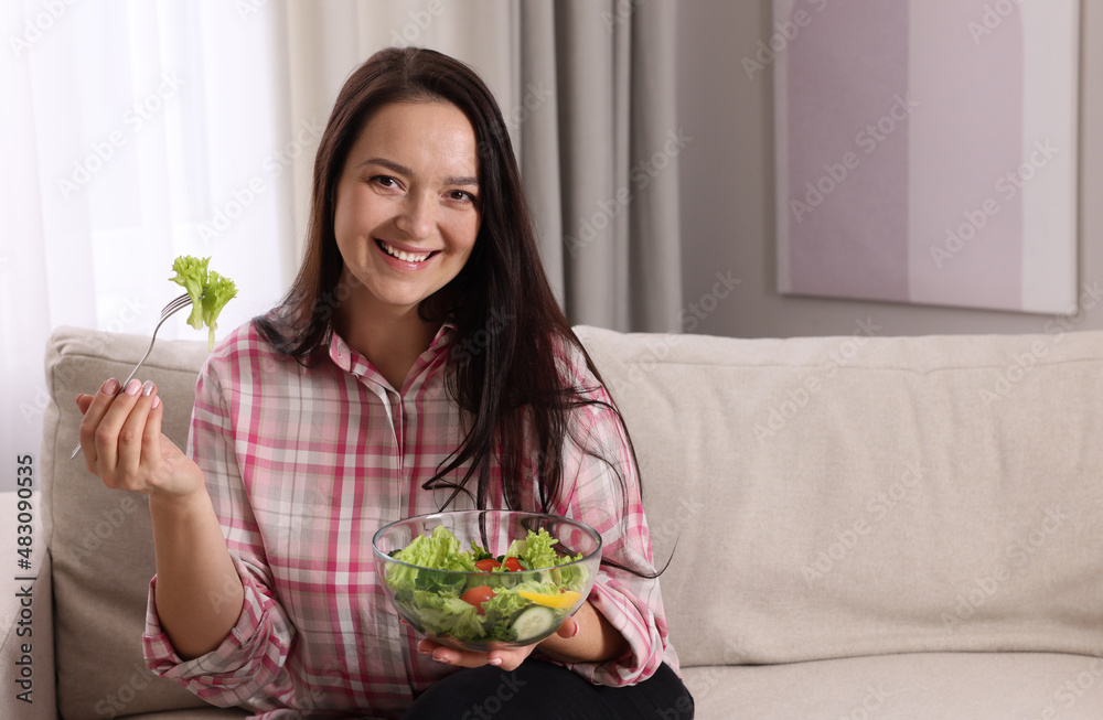 Beautiful overweight woman eating salad in living room, space for text. Healthy diet Beautiful overweight woman eating salad in living room, space for text. Healthy diet