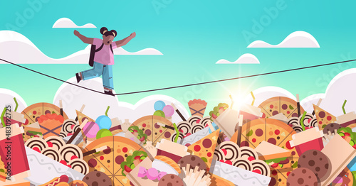 schoolgirl balancing on rope above junk food assortment of fast food unhealthy nutrition junkfood addiction