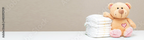 Stack of diapers for baby, toddler with toy teddy bear on table. set for boy girl for baby shower with copy space, banner