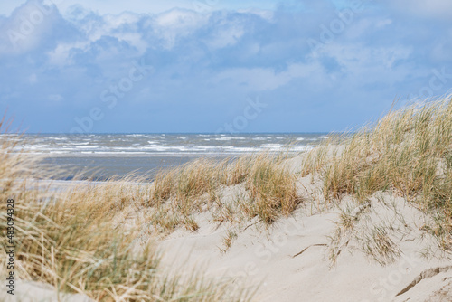 Beach on the North Sea. Small dune with grass and with the North Sea in the background. At the sea in a German travel destination. Promenade in the Netherlands. Vacation in spring 
