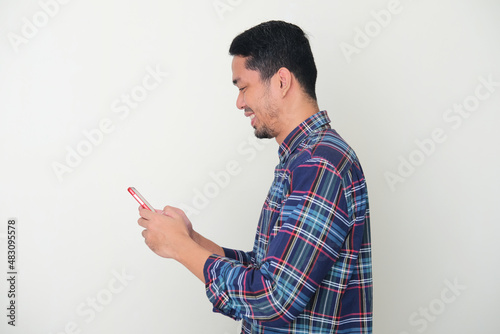 Side view of Adult Asian man looking to his mobile phone with happy expression photo