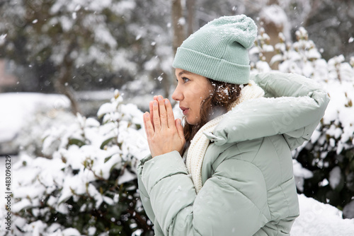 Young woman warming her hands on the street in snowy cold day. photo