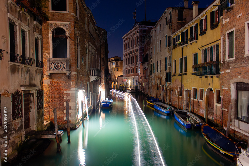 Canal in Venice with the lights of a passing boat. Long exposure at night.