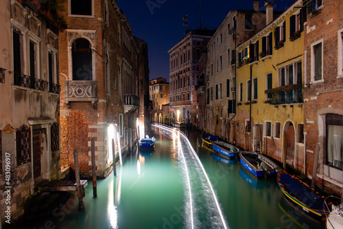 Canal in Venice with the lights of a passing boat. Long exposure at night. © Alican