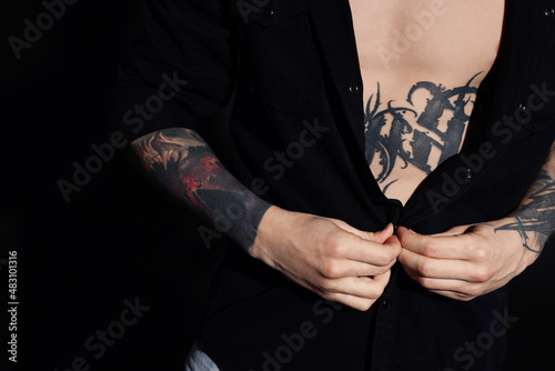 Young man with tattoos wearing black shirt on dark background  closeup