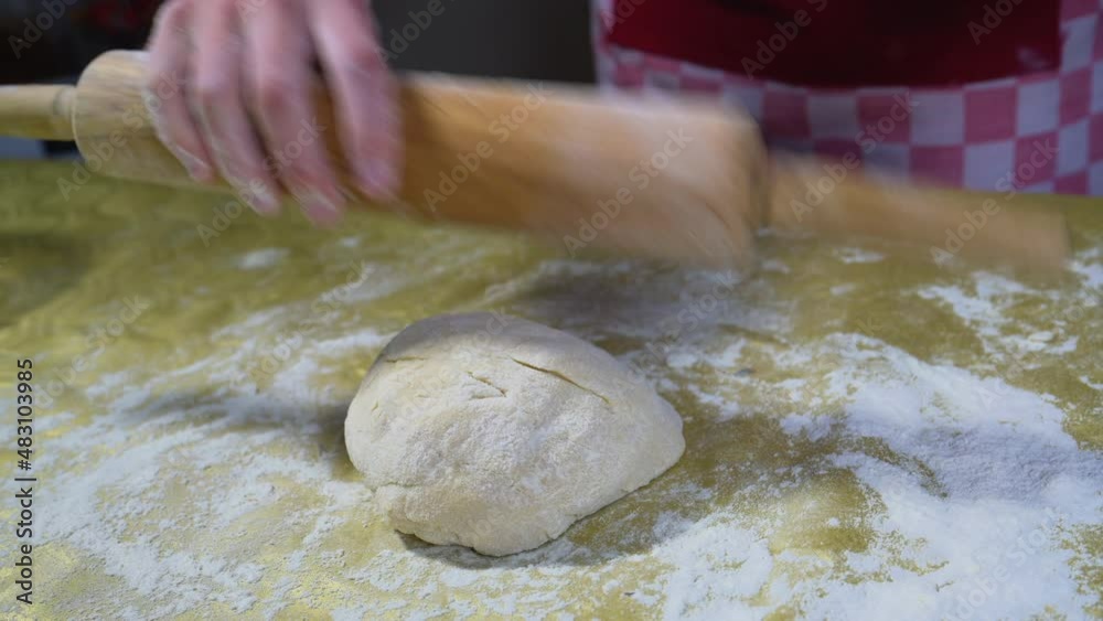 Baker rolls out the dough with a rolling pin on the table. The process of preparing and whipping dough. Selective Focus