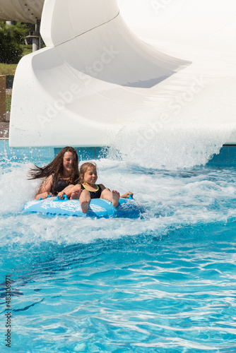 Excited girls ride water slide. Water park holiday time.