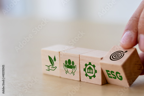 ESG concept of environmental, social and governance. Sustainable corporation development. Hand flips wooden cubes with target setting  to ESG icon with other ESG icons on bright background.Copy space. photo