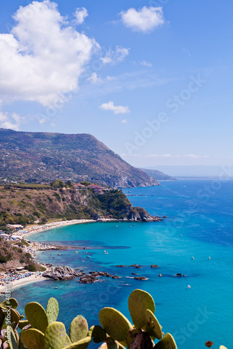View of turquoise gulf bay, sandy beach, green mountains and plants, blue sky white clouds