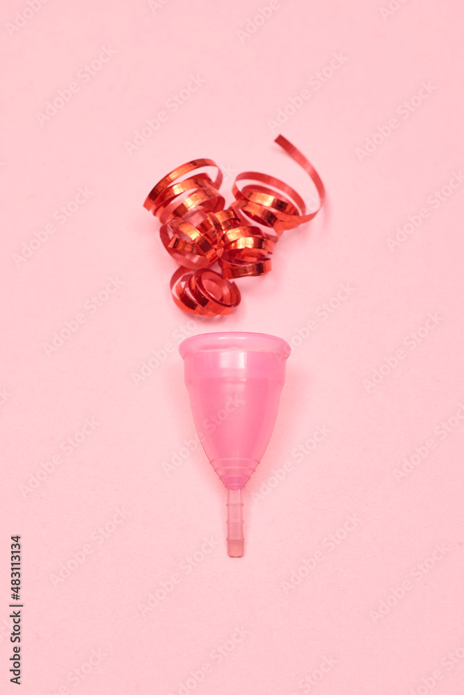Pink menstrual cup on pink background. Decorated with red ribbon. Pink menstrual cup on pink background. Decorated with red ribbon.