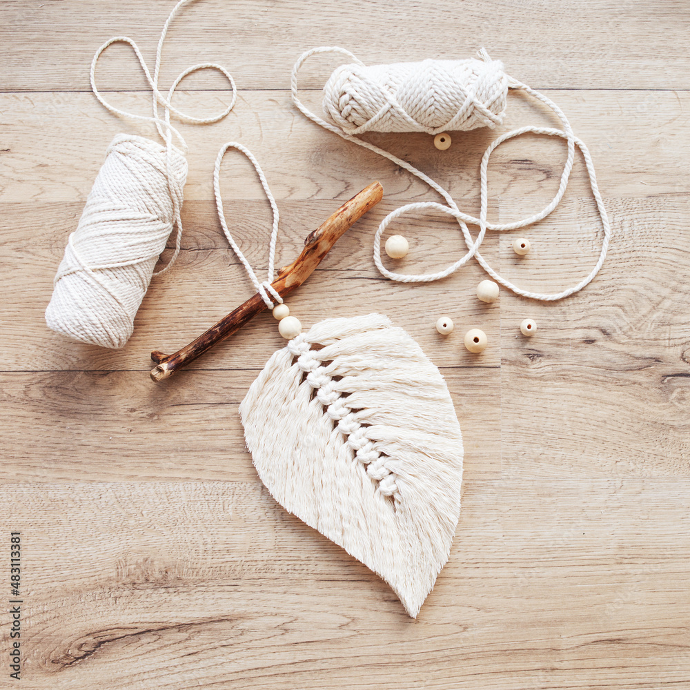 Macrame leaf in natural color and thread windings lying on a wooden table. Cotton rope decor macrame to make your room more cozy and unique. Woman hobby. Handmade wall hanging decor. Copy space Macrame leaf in natural color and thread windings lying on a wooden table. Cotton rope decor macrame to make your room more cozy and unique. Woman hobby. Handmade wall hanging decor. Copy space