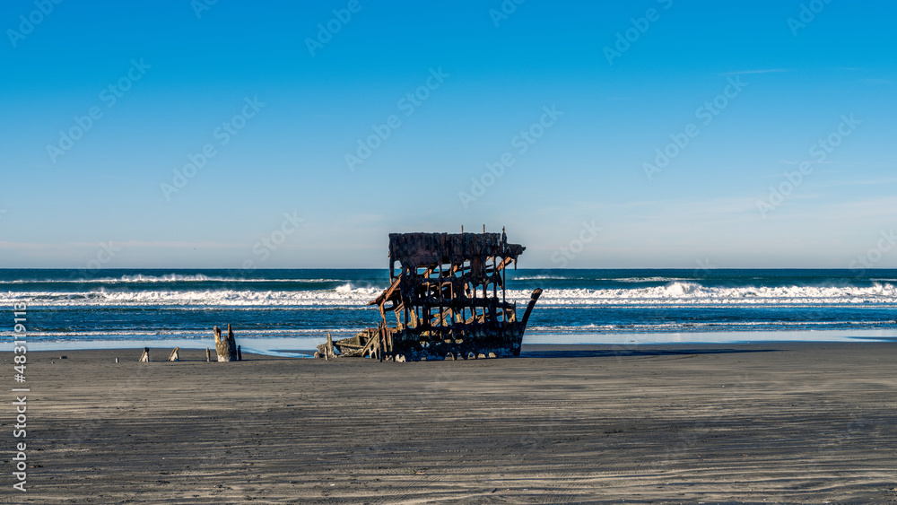 Shipwreck in the sandy beach at Fort Stevens in Northern Oregon with incoming waves and a bright blue sky and copy space. Shipwreck in the sandy beach at Fort Stevens in Northern Oregon with incoming waves and a bright blue sky and copy space.
