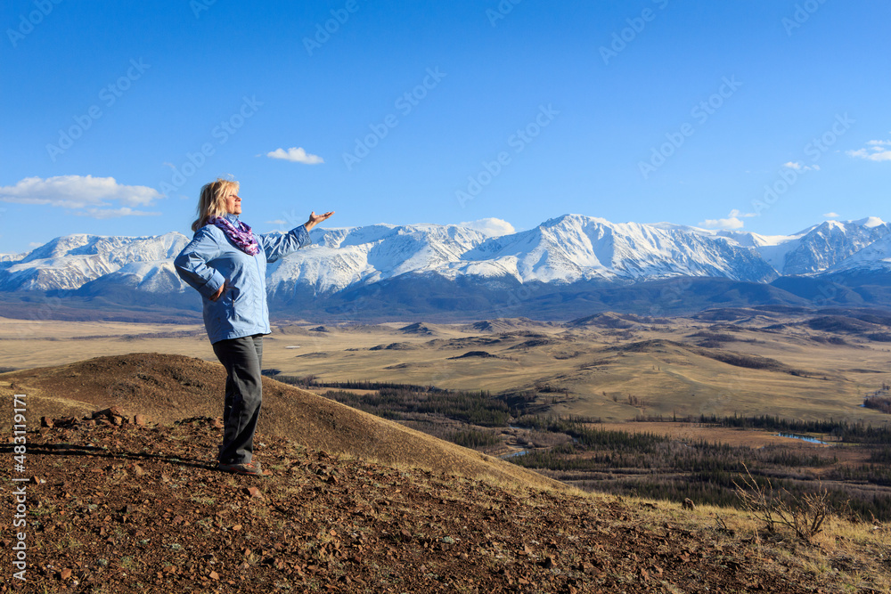 Naklejka premium a female tourist invites you to the mountains with a view of the snowy peaks of Altai