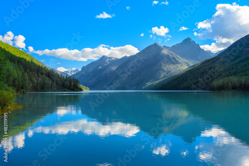 Kucherlinsky Lake of the Altai Mountains during the day in sunny weather with mountain peaks reflected in the water and a blue sky with clouds