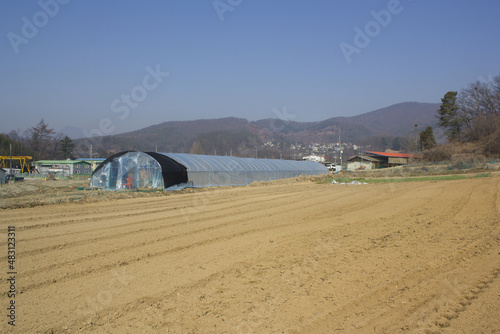 It is a well plowed winter field with a view of the green house.