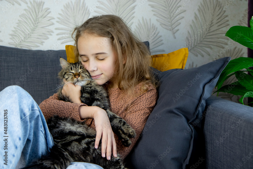 a little blonde girl sits on a sofa and hugs a gray tabby cat tightly, communication, care and life with pets