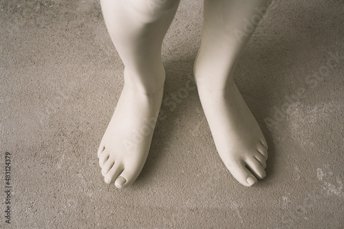 Close-up of a white-gray leg of a mannequin on a concrete pavement.