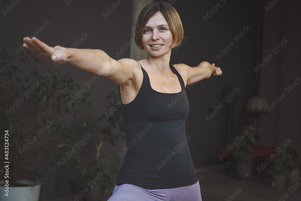 Young woman performing Virabradrasana 2 or warrior pose 2 at home. Yoga instructor at doing stretching poses at modern home interior. Healthy life style concept.