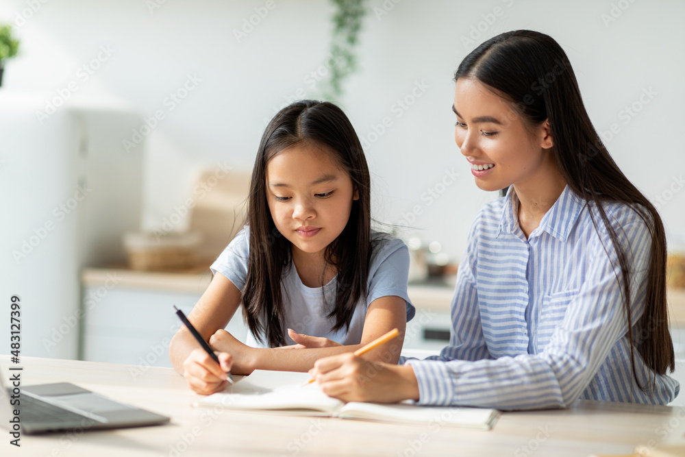 Caring asian mother assisting to daughter with her homework, spending time in kitchen at home, free space Caring asian mother assisting to daughter with her homework, spending time in kitchen at home, free space
