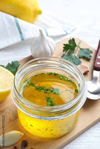 Jar with lemon sauce and ingredients on white wooden table, closeup. Delicious salad dressing