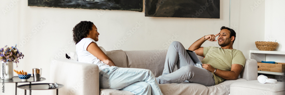 Middle eastern man and woman smiling and talking while resting on couch