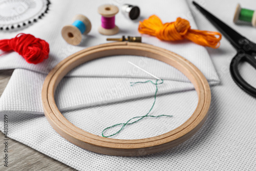 Embroidery hoop, fabric and other accessories on wooden table photo