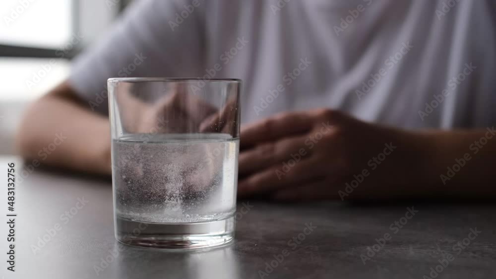 a man is waiting for an aspirin tablet to dissolve in a glass of water close-up a man is waiting for an aspirin tablet to dissolve in a glass of water close-up
