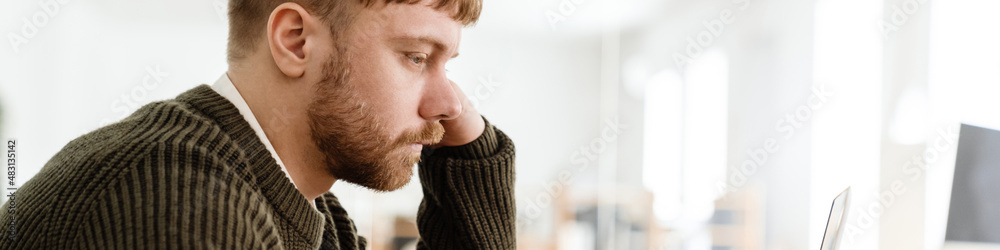 Obraz premium Young ginger man working with laptop while sitting at table in office