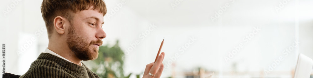 Fototapeta premium Young ginger man gesturing and working with laptop while in office