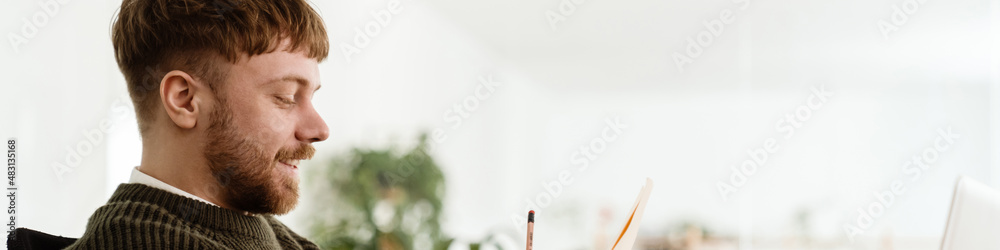 Obraz premium Young ginger man working with laptop while sitting at table in office