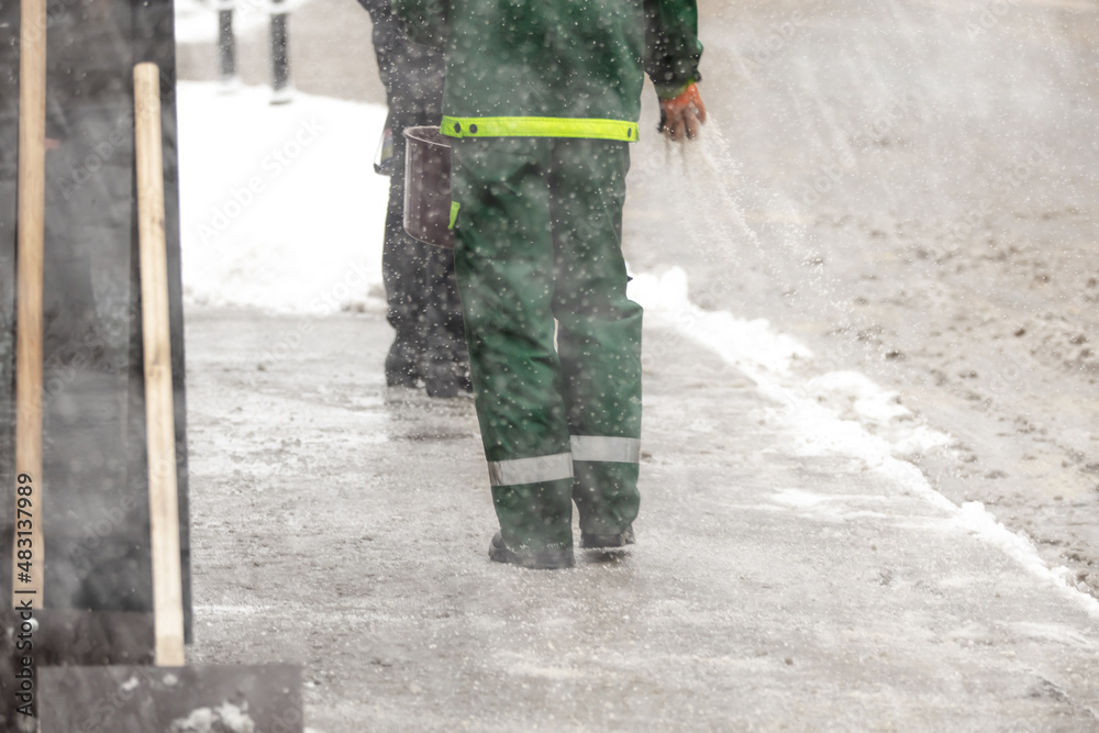 Public worker service putting salt on icy sidewalk during heavy snowfall. Public worker service putting salt on icy sidewalk during heavy snowfall.