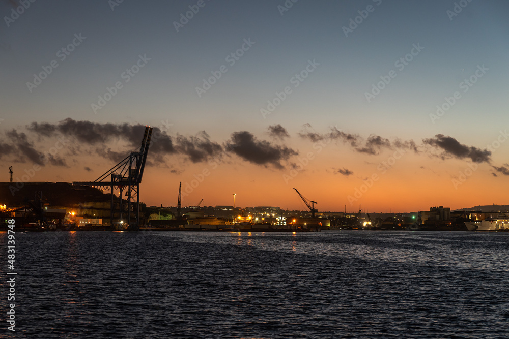 Sunset over the harbor of Valletta, Malta with sea cranes and an orange sky