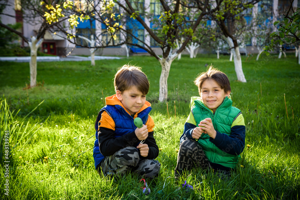 Kids on Easter egg hunt in blooming spring garden. Children searching for colorful eggs in flower meadow. Toddler boy and his brother friend kid boy play outdoors