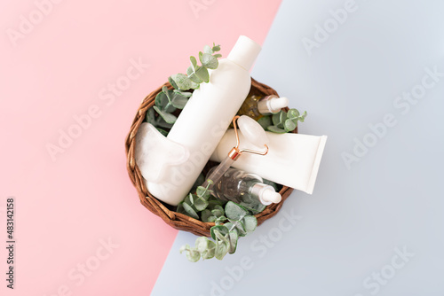Massage stone roller and bottles with facial serum with natural organic beauty oil for cosmetic skin care, natural braided tray and flower leaves