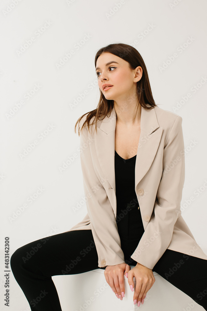Young woman in trendy pastel suit sitting on cube against white background Young woman in trendy pastel suit sitting on cube against white background