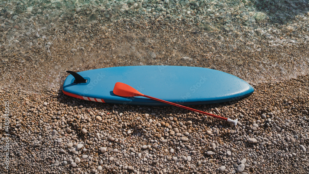Blue SUP board and paddle for surfing on stony shore Blue SUP board and paddle for surfing on stony shore
