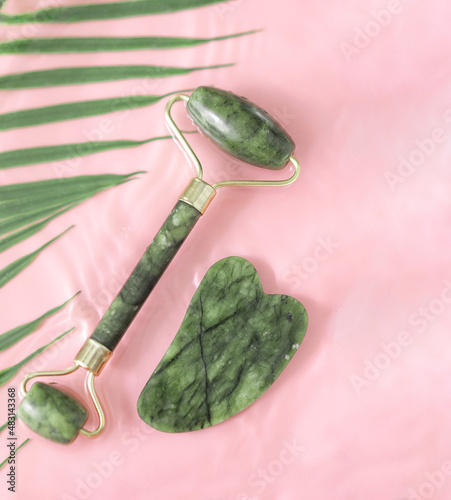 Jade facial roller for cosmetic facial massage, natural stone skin care products. It lay flat on a pink background. The water rings, splashes. glare from the water. A place to copy, a place for text.