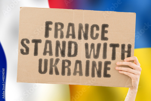 The phrase " France stand with Ukraine " on a banner in men's hand with blurred French and Ukrainian flag on the background. Team. European. War. Assistance. Negotiation. Safety. Security