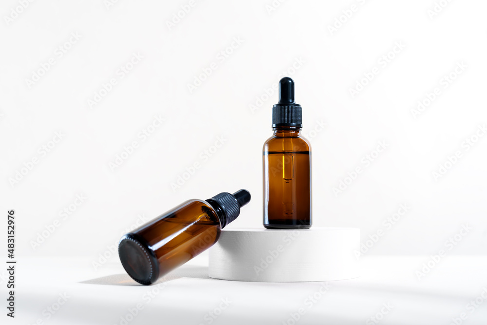 Glass dropper bottles with a pippette with black rubber tip on the white circle podium background. Nature Skin concept. Organic Spa Cosmetics. Trendy concept. Glass dropper bottles with a pippette with black rubber tip on the white circle podium background. Nature Skin concept. Organic Spa Cosmetics. Trendy concept.