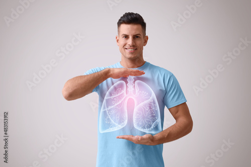 Handsome man holding hands near chest with illustration of lungs on grey background photo