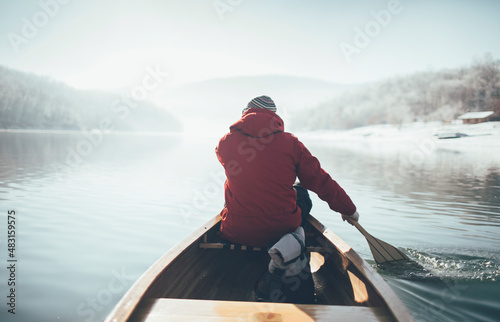 Rear view of man paddling canoe on the winter sunny day