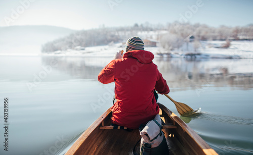 Rear view of man in red jacket paddling canoe on lake winter ride photo