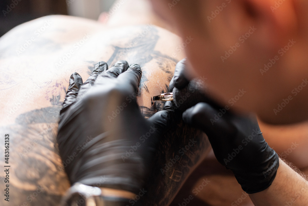 man tattoo artist with black gloves with a tattoo machine drawing a tattoo on a man's body, close-up