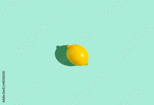 Fresh yellow whole one lemon in center of minimal blue background on bright sun light with hard shadow summer concept flat lay from above, citrus food composition