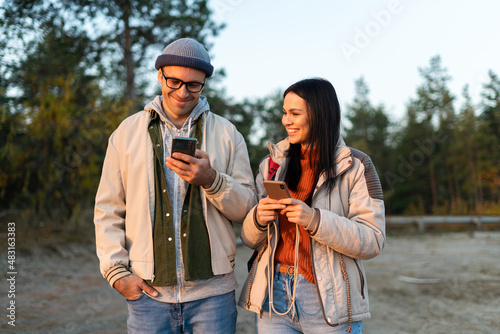 Waist up portrait view of the caucasian man looking at the smartphone screen while bonding to his woman with forest at the background