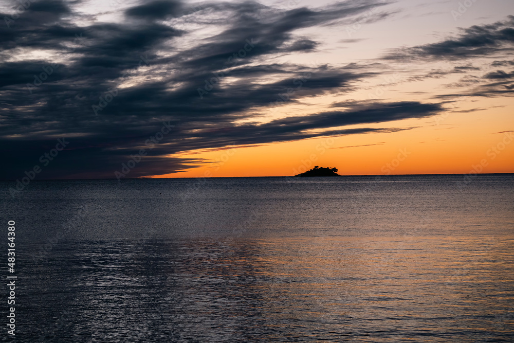 Amazing sunset above the distant island off the Rovinj shore with rain clouds approaching over horizon