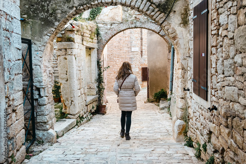 Girl wandering through the old  stone alleys of Istrian town of bale during cold weather  dressed in winter jacket