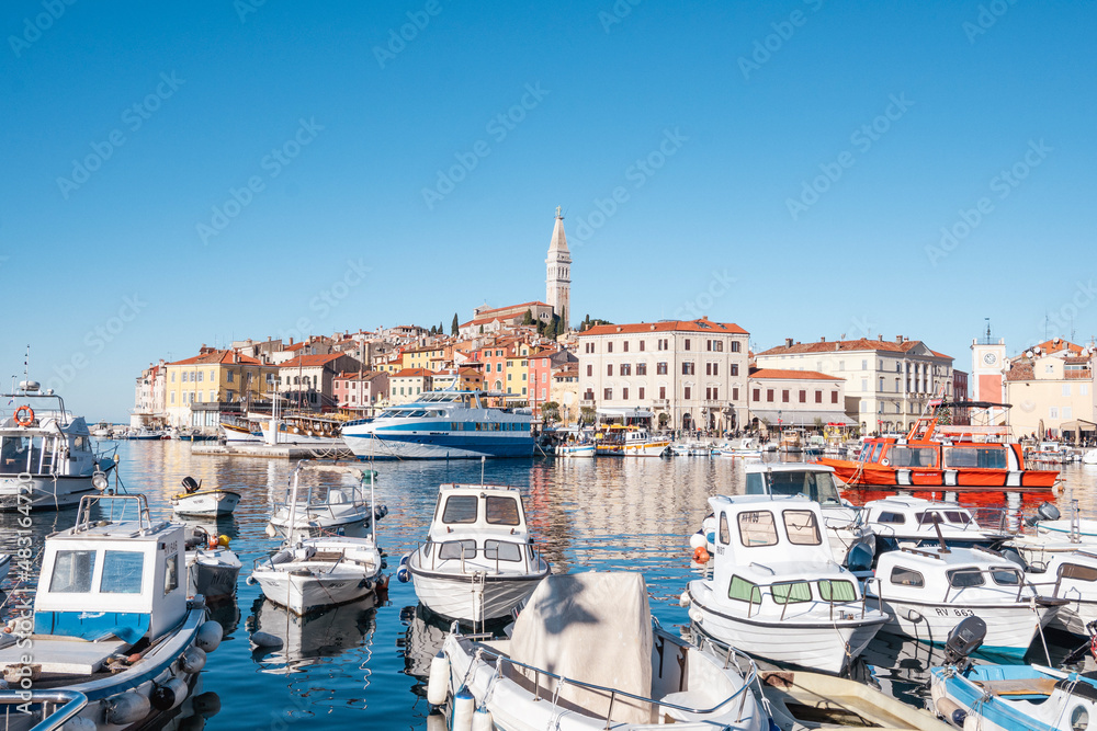 Beautiful fishing boats anchored in the Rovinj city port, Istria, Croatia, during crystal clear winter morning, lit by gentle sun with St. Euphemia church rising above the houses